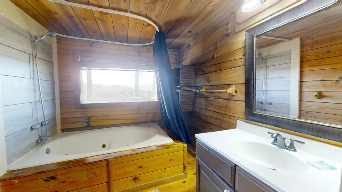 A tranquil bathroom with a jacuzzi tub set beside a large window. Wooden walls, a mirror, and gentle natural light create a soothing, spa-like ambiance—ideal for unwinding after days spent hiking or exploring nearby attractions.