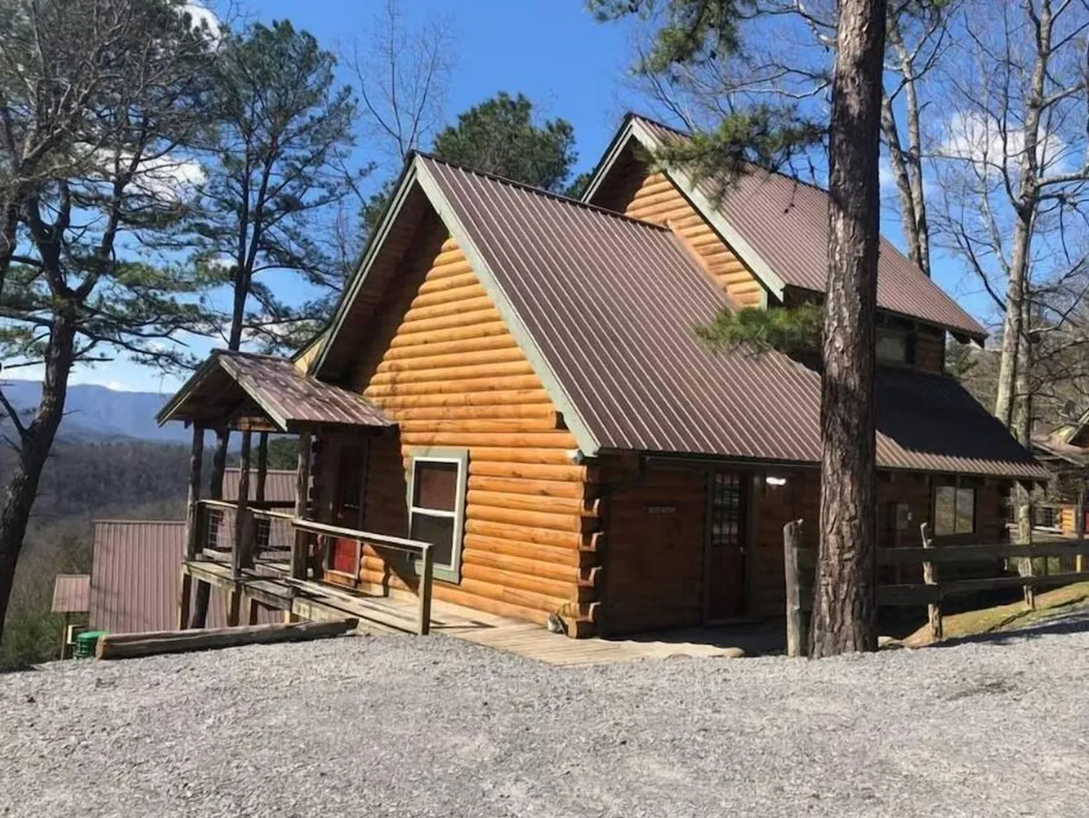 This image showcases the exterior of a charming log cabin nestled among trees. The front porch invites relaxation and hints at family gatherings or quiet mornings with a view. The surrounding natural landscape emphasizes proximity to outdoor adventure opportunities.