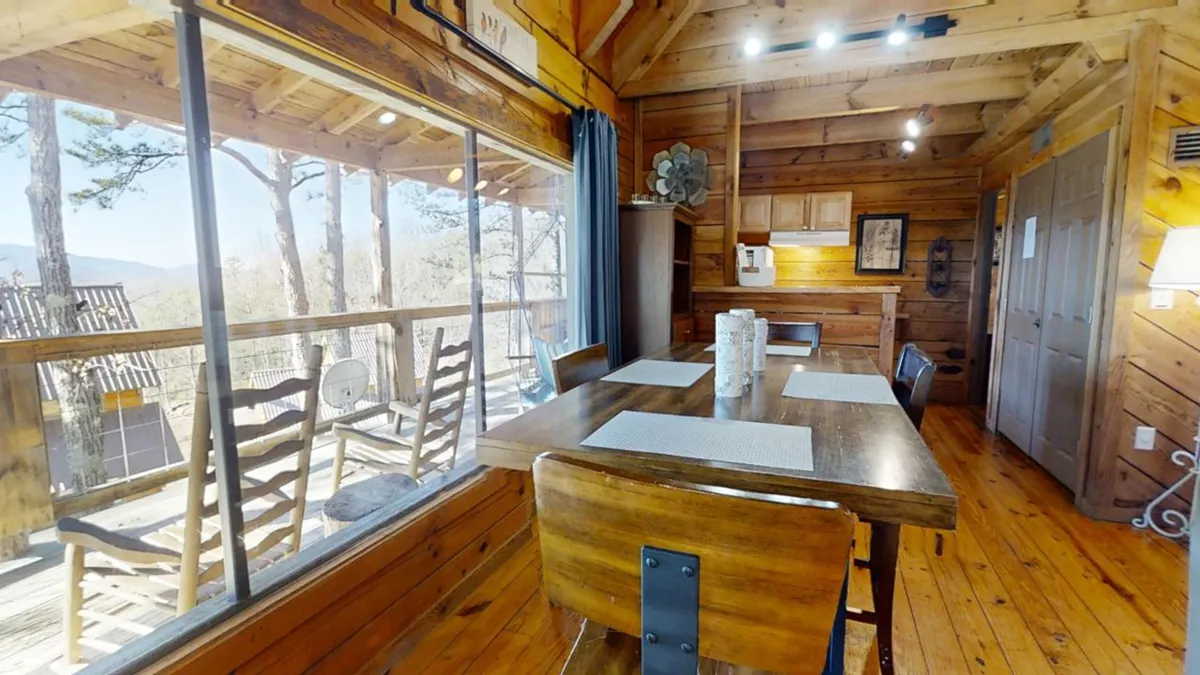 The photo captures a dining table surrounded by large windows and rustic wooden beams, creating a warm, communal setting. The atmosphere is bright and friendly, perfect for shared meals, planning adventures, and stretching vacation dollars.