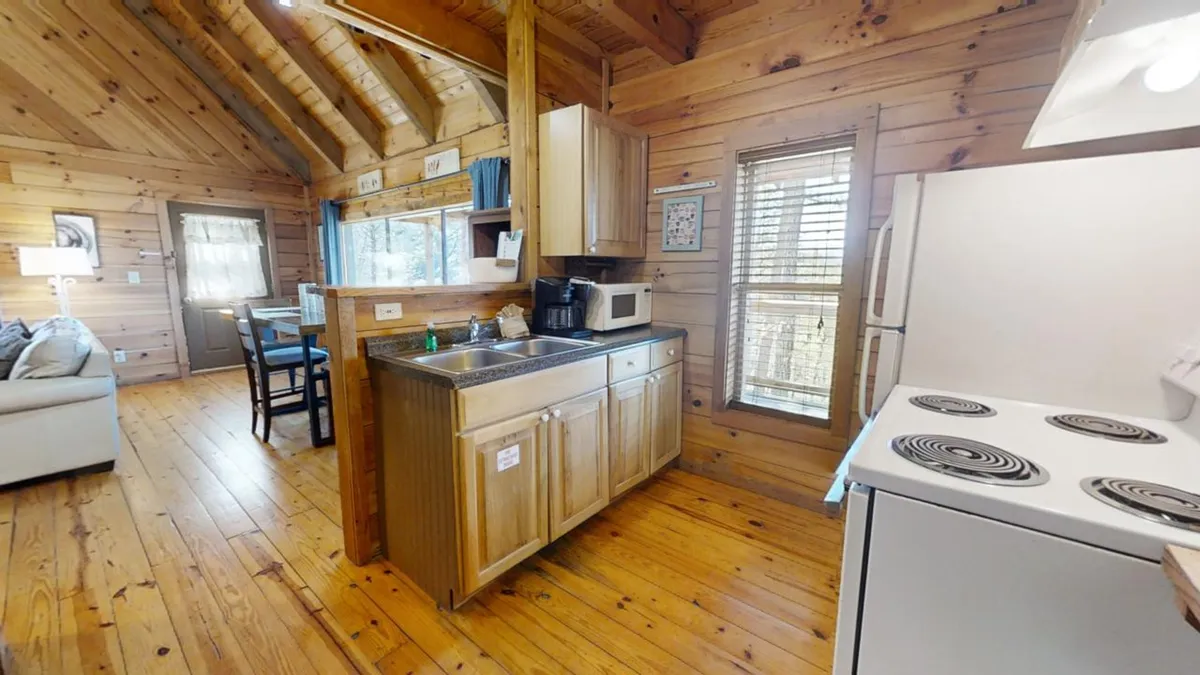 This picture features a kitchen sink with wooden cabinets, a window with blinds letting in natural light, and a stove within easy reach. The setting feels intimate and practical, ideal for both everyday cooking and creating special family memories.