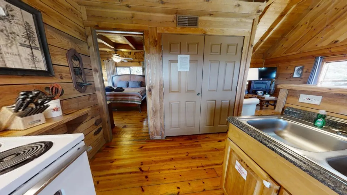 The scene captures a welcoming kitchen area with wooden cabinetry, a window letting in natural light, and a glimpse of an adjacent bedroom. The mood is inviting and communal, suggesting family meals and shared moments after a day outside.