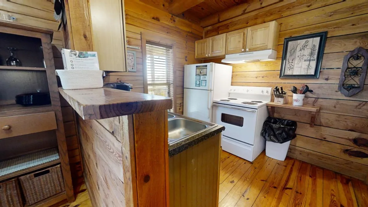 The image showcases a warmly lit kitchen with a roomy countertop, white modern appliances, wooden cabinets, and wooden floors. The space is organized and inviting, hinting at a fully equipped area ready for meal preparation, family gatherings, or casual entertaining.